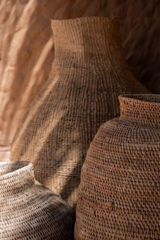 Hand-woven vessels against a textured earth wall in warm light.